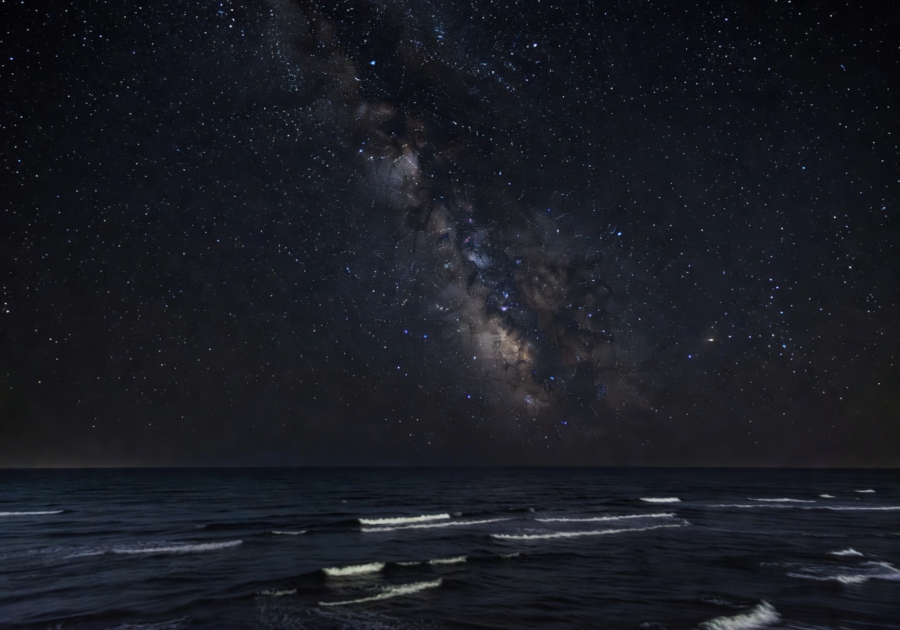 Night sky full of stars above dark ocean